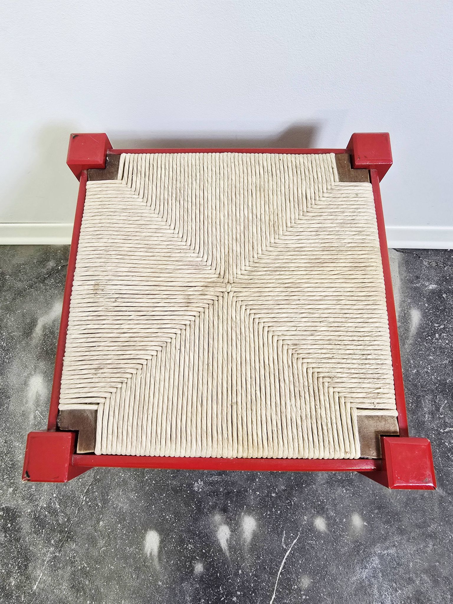 Red wooden stool with a woven straw seat.