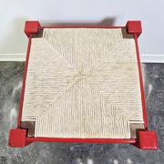 Red wooden stool with a woven straw seat.