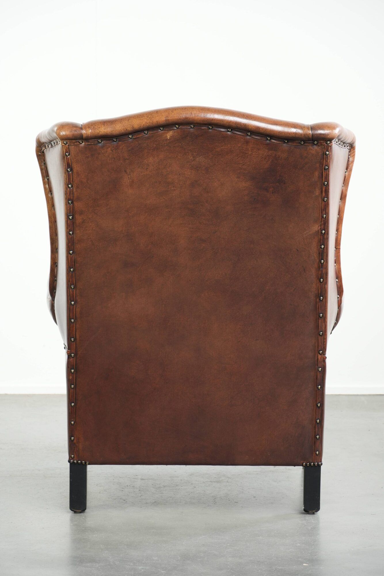 Sheepskin wingback armchair in a warm cognac colour with refined nailhead trim