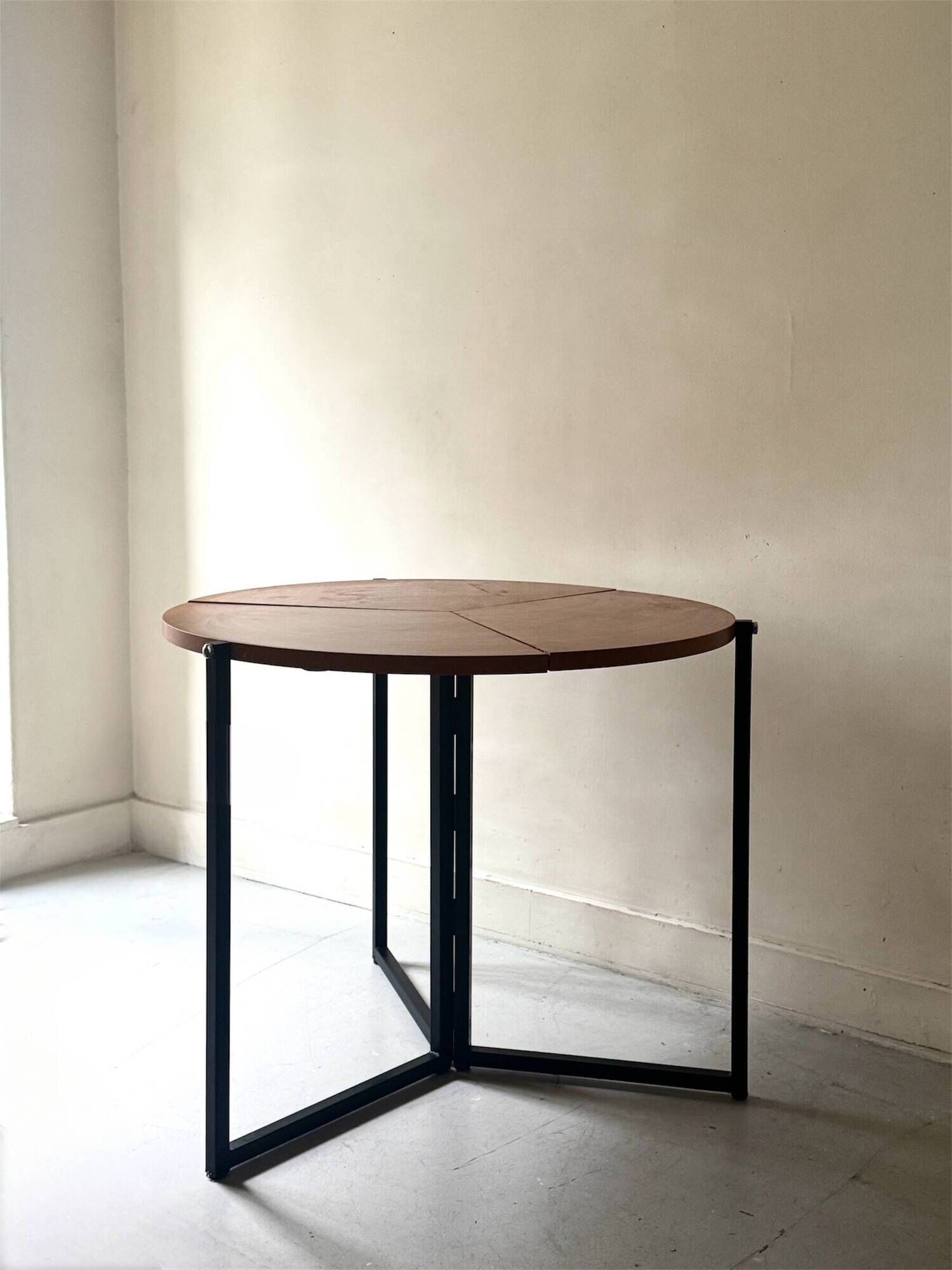 Modernist round folding dining table in wood and metal.
