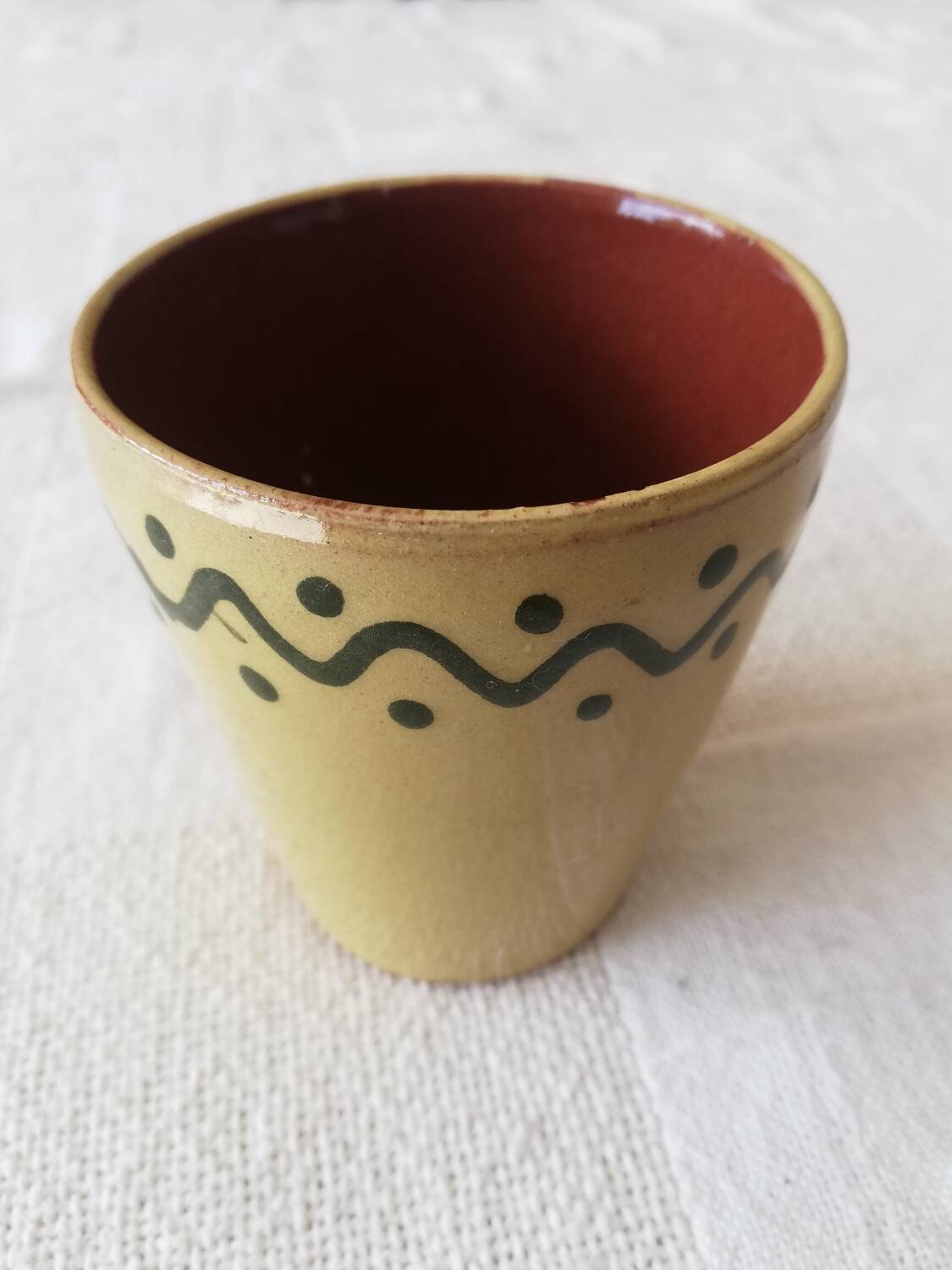 Mustard-colored ceramic cup or glass with green decor