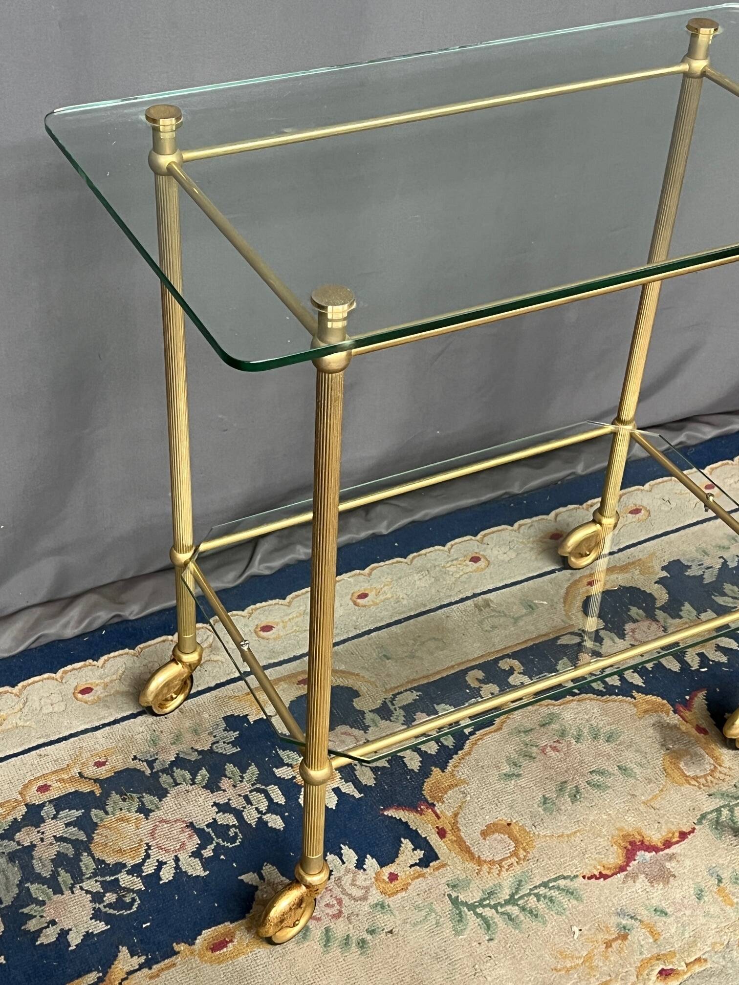 Service trolley on wheels with two glass shelves and a brass frame.