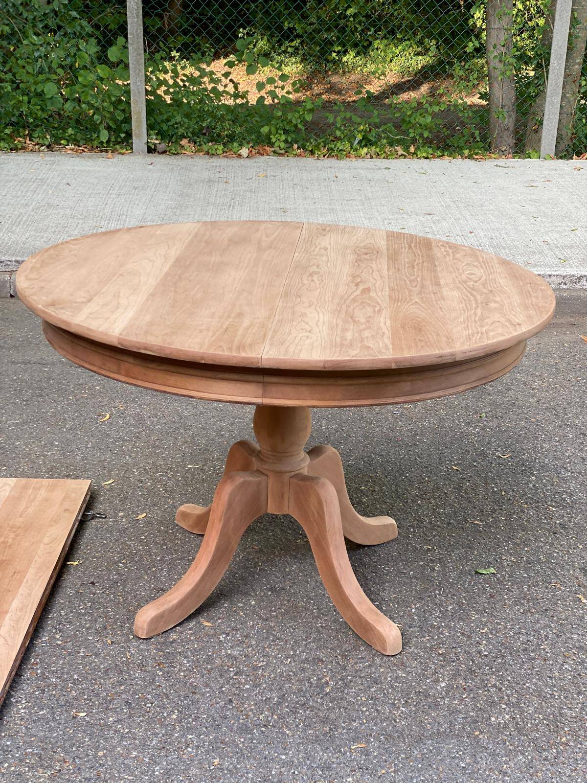 Large extendable round dining table stripped in solid cherry wood with a central leg.