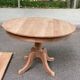 Large extendable round dining table stripped in solid cherry wood with a central leg.