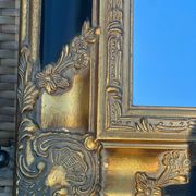 Miroir Baroque en bois doré sur fond noir.