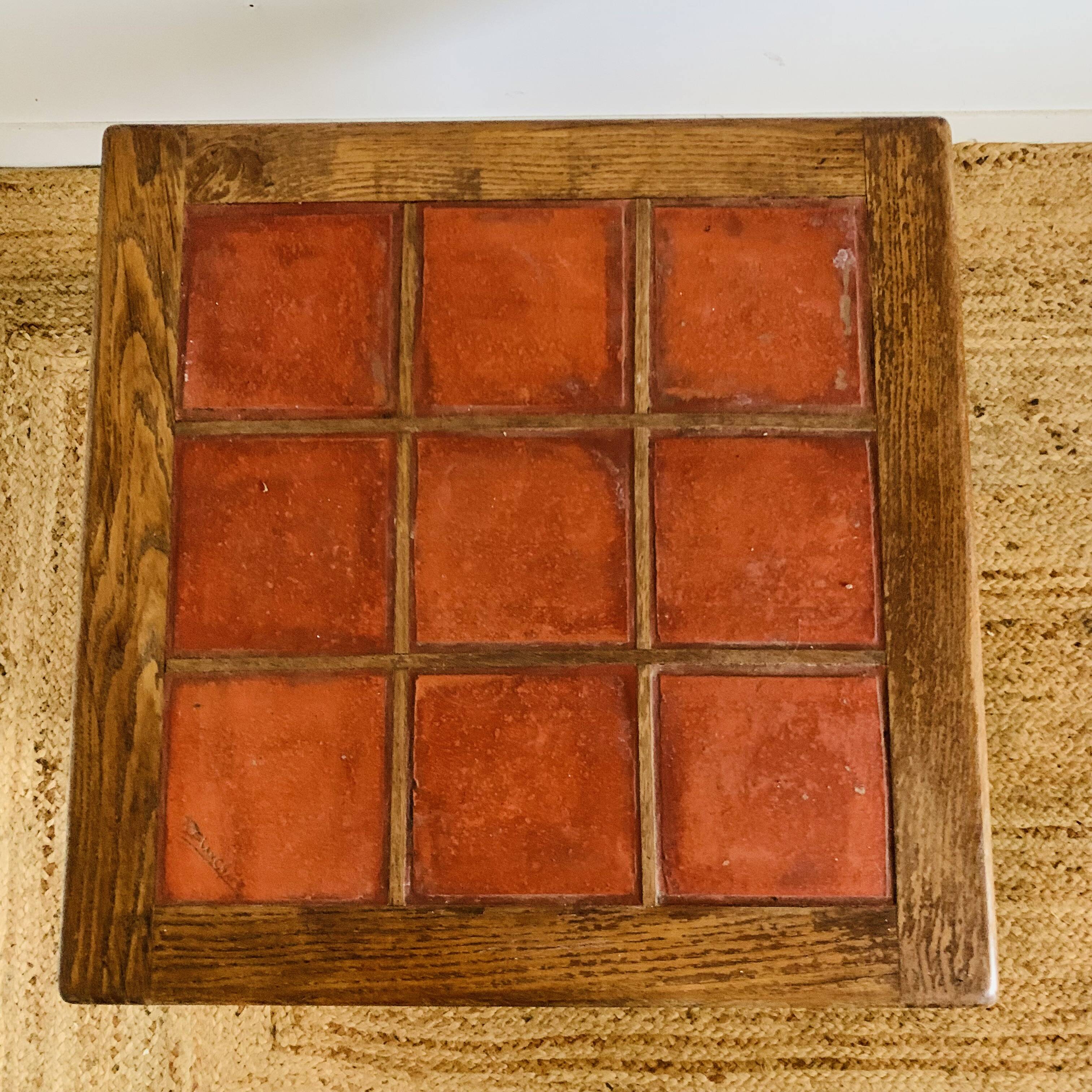 Square table with red tiles signed.