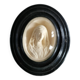 Religious medallion of the Virgin Mary in a blackened wooden frame.