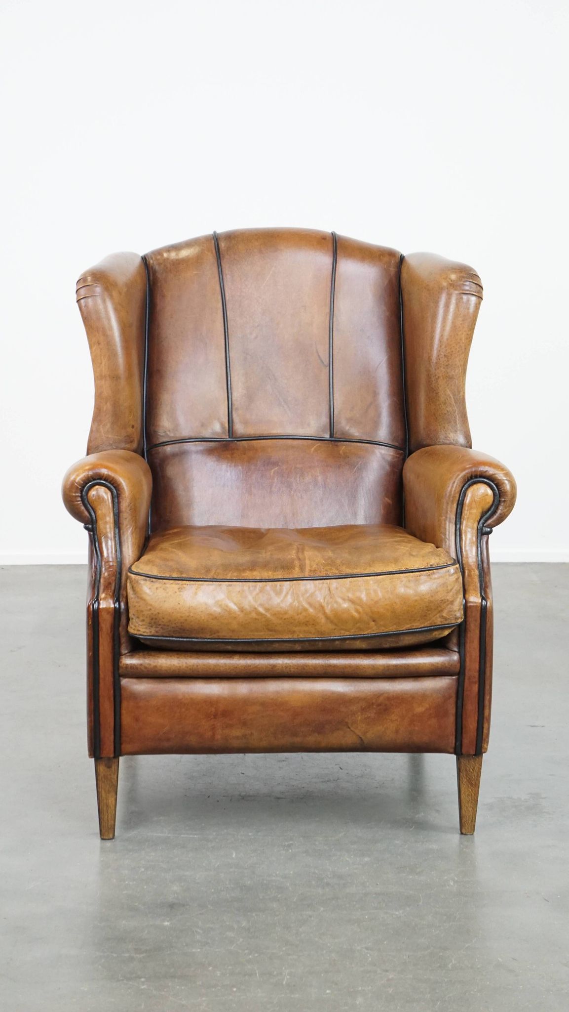 Cognac-colored sheep leather wingback chair finished with black piping