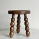 Small three-legged stool made of turned wood.