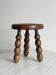 Small three-legged stool made of turned wood.