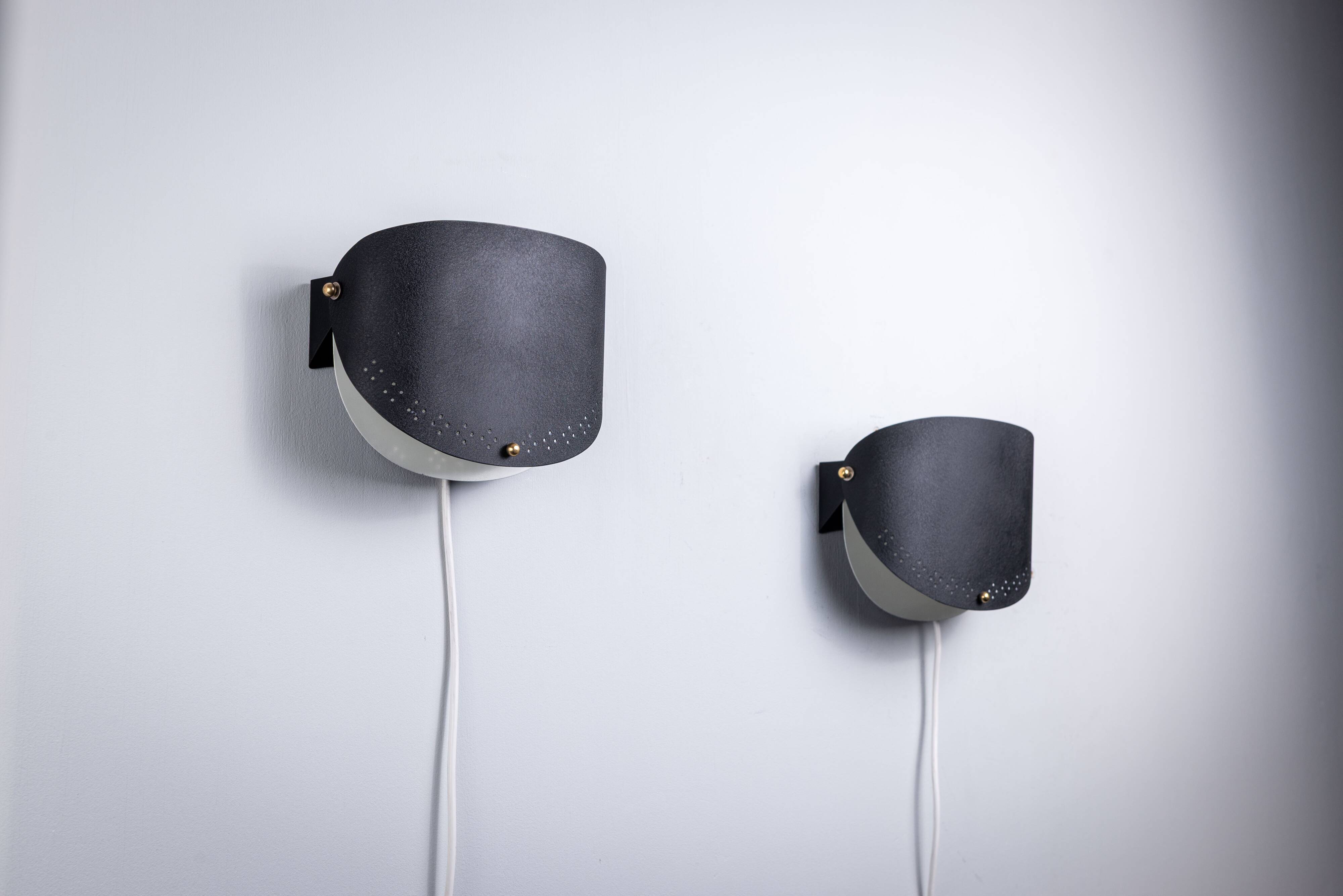 Matte black wall lamps with perforated shades and brass details