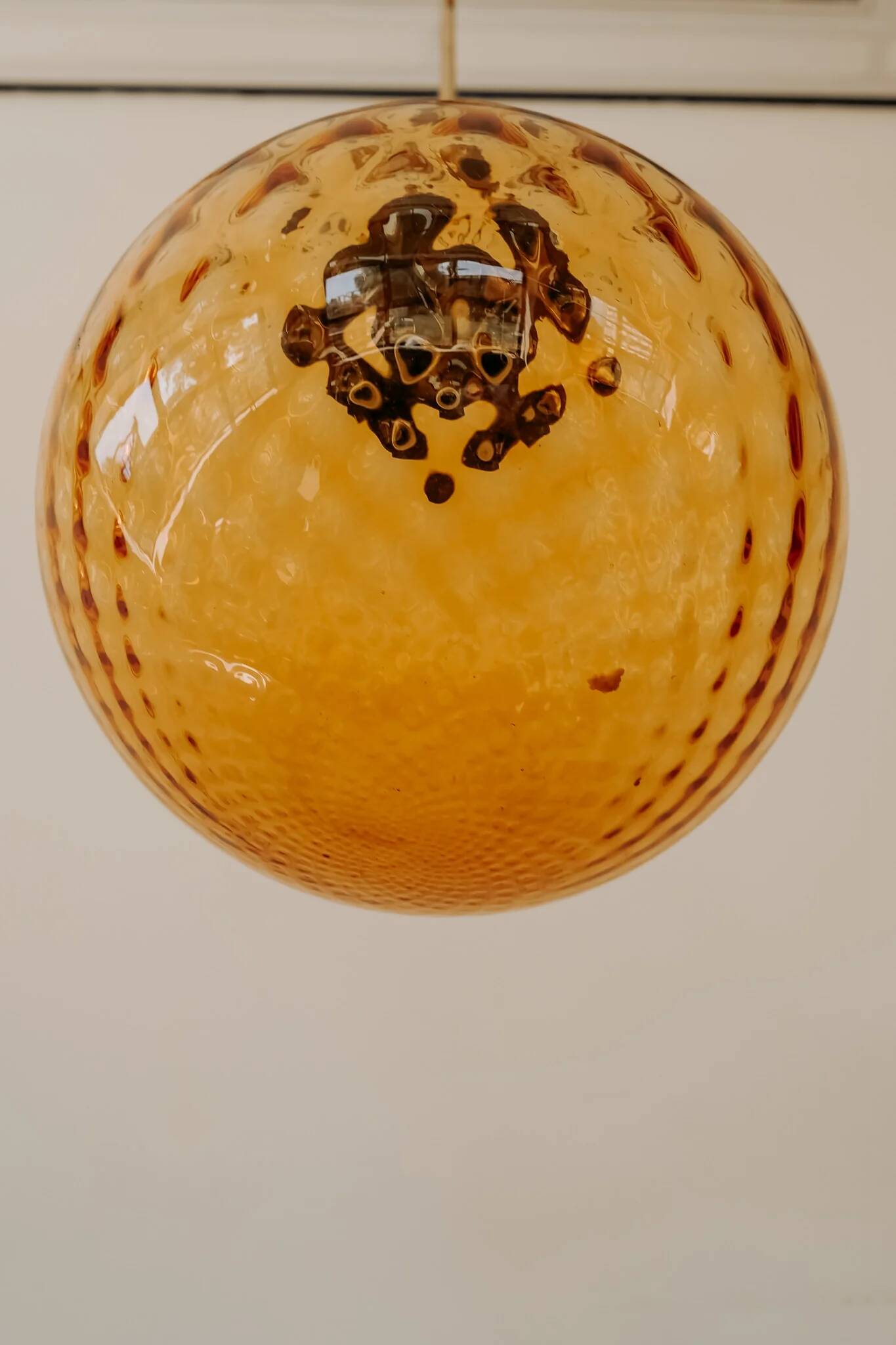 Brass pendant light with a round orange glass shade and a swirling structure.