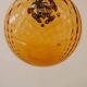 Brass pendant light with a round orange glass shade and a swirling structure.