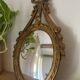 Oval convex witch mirror with golden ribbon mouldings.
