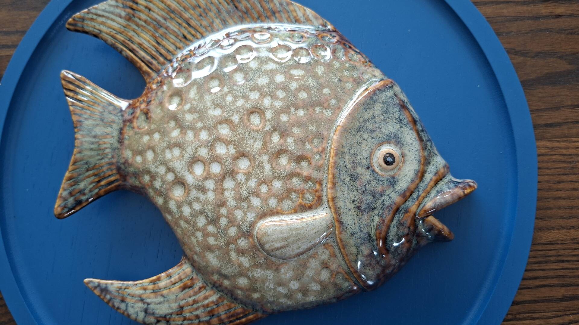 Vallauris ceramic wall sculpture of a relief fish on a blue plaque.