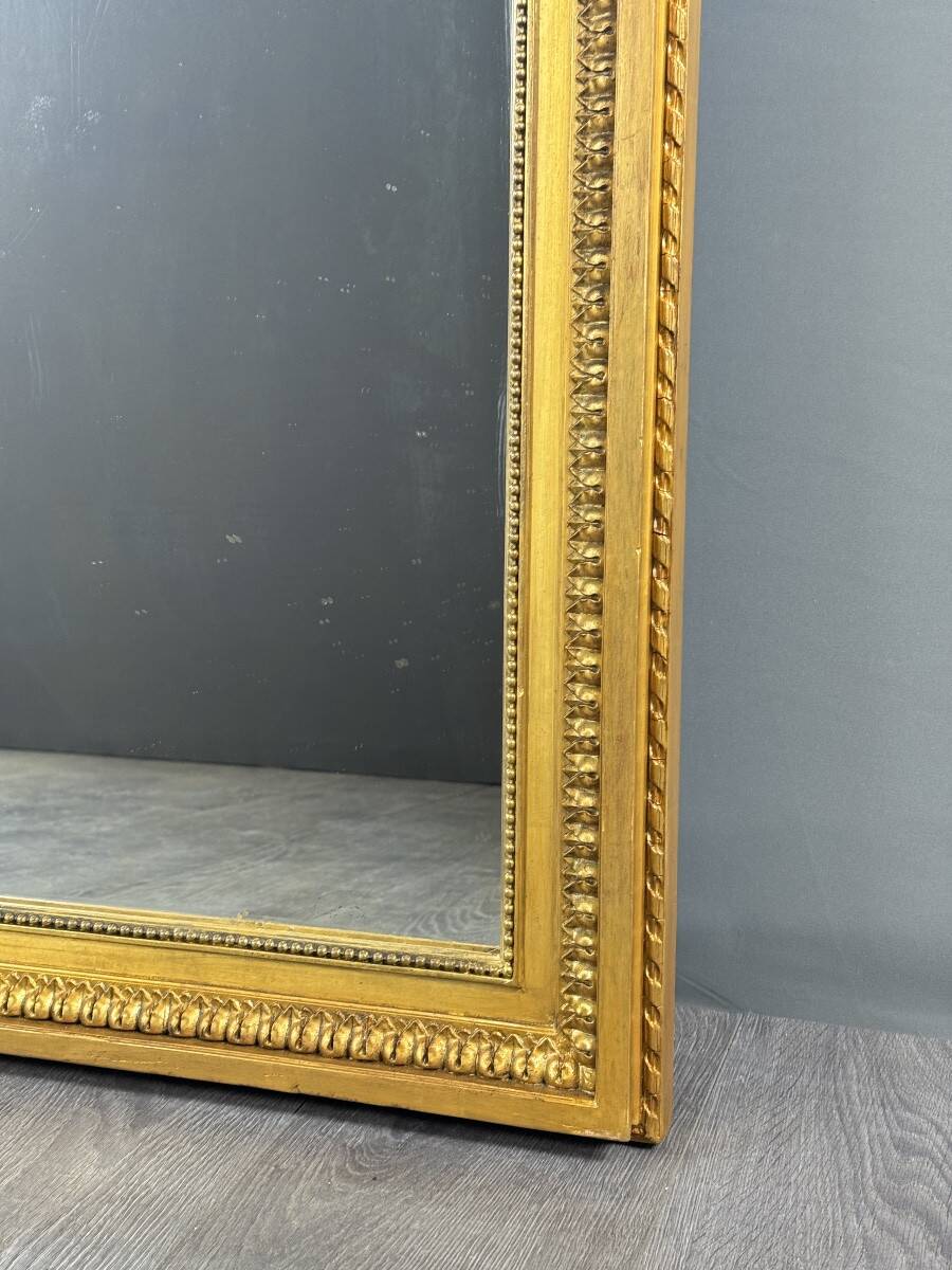 Large antique gilded wooden mirror in Louis XVI style with a sculpted pediment, 19th century.