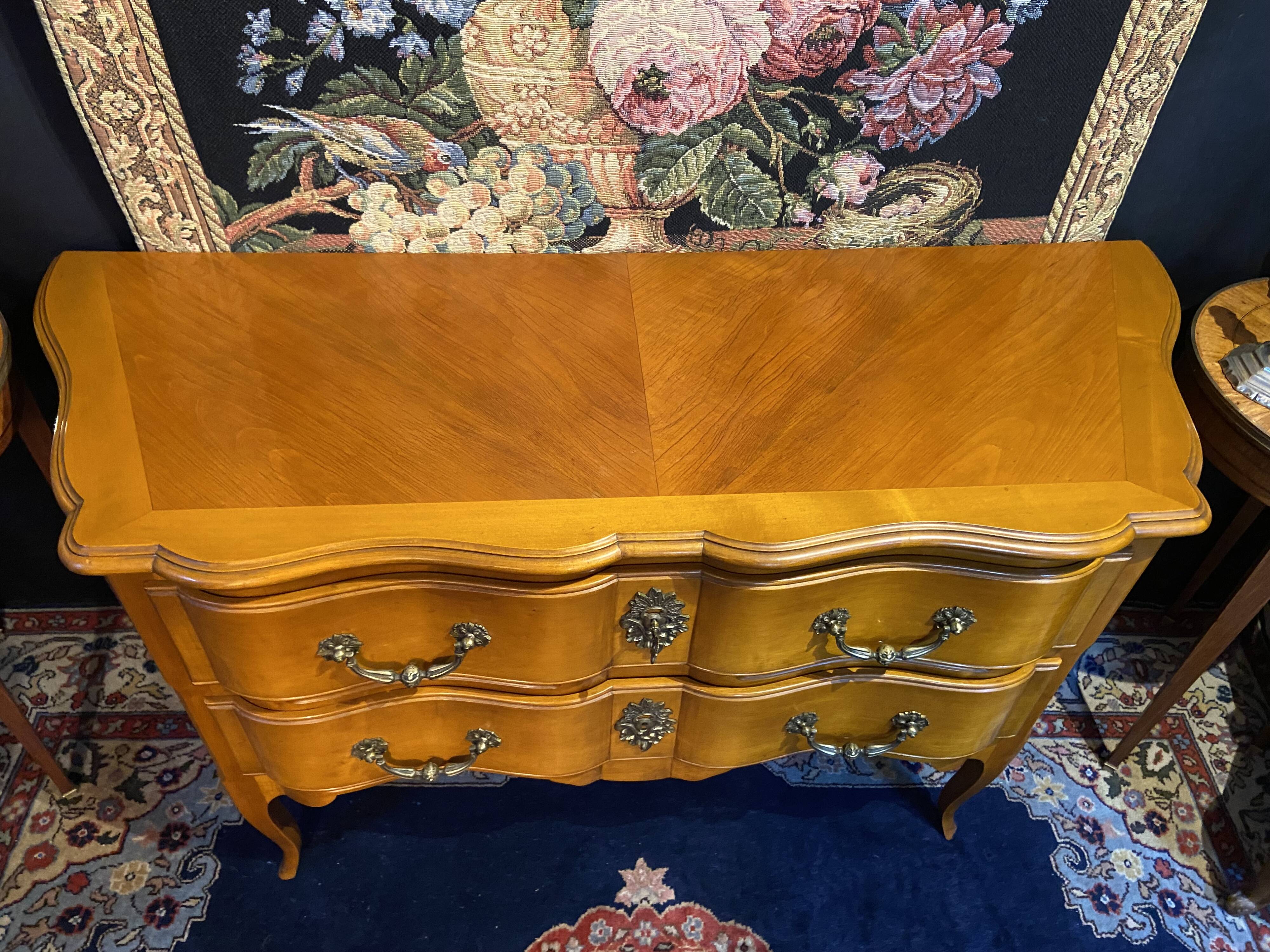 Large bow-fronted chest of drawers in blonde cherry with bronze ornamentation.