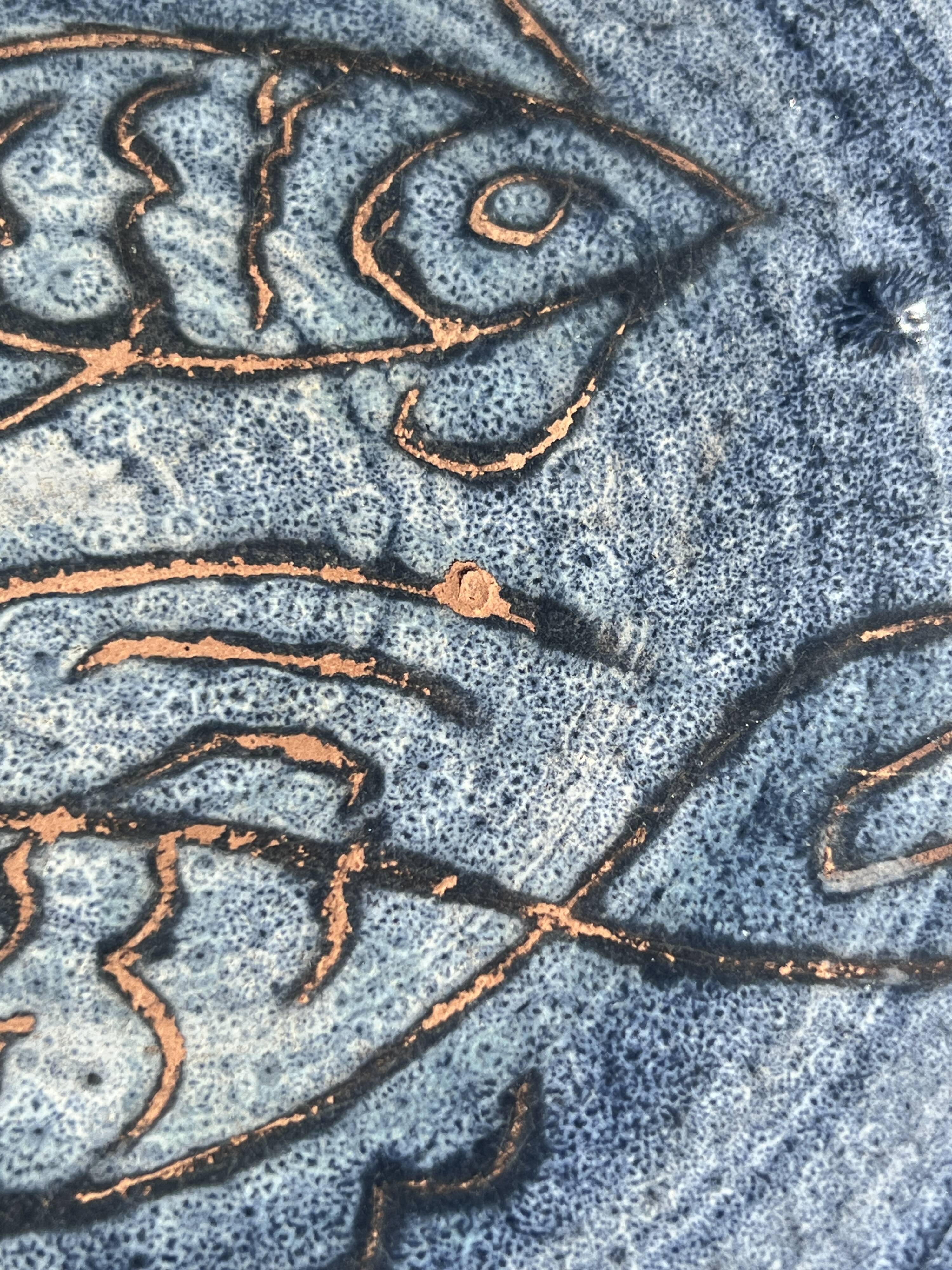 Glazed blue ceramic bowl with stylised fish decoration.