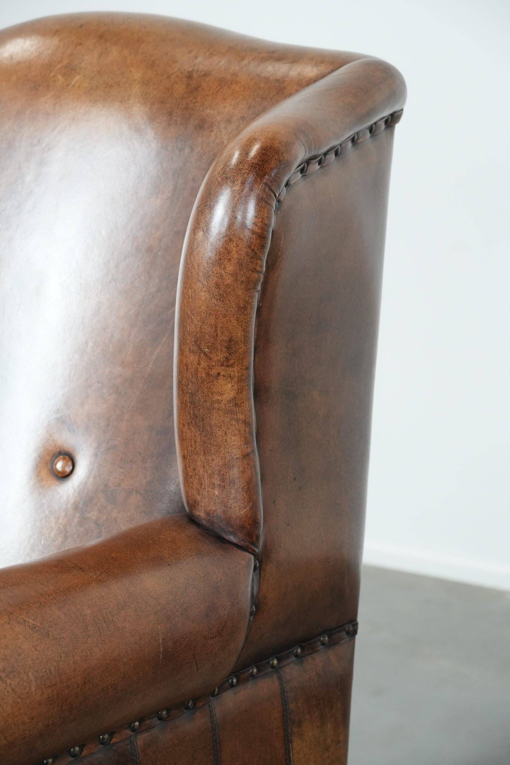 Sheepskin wingback armchair with decorative nails and black piping