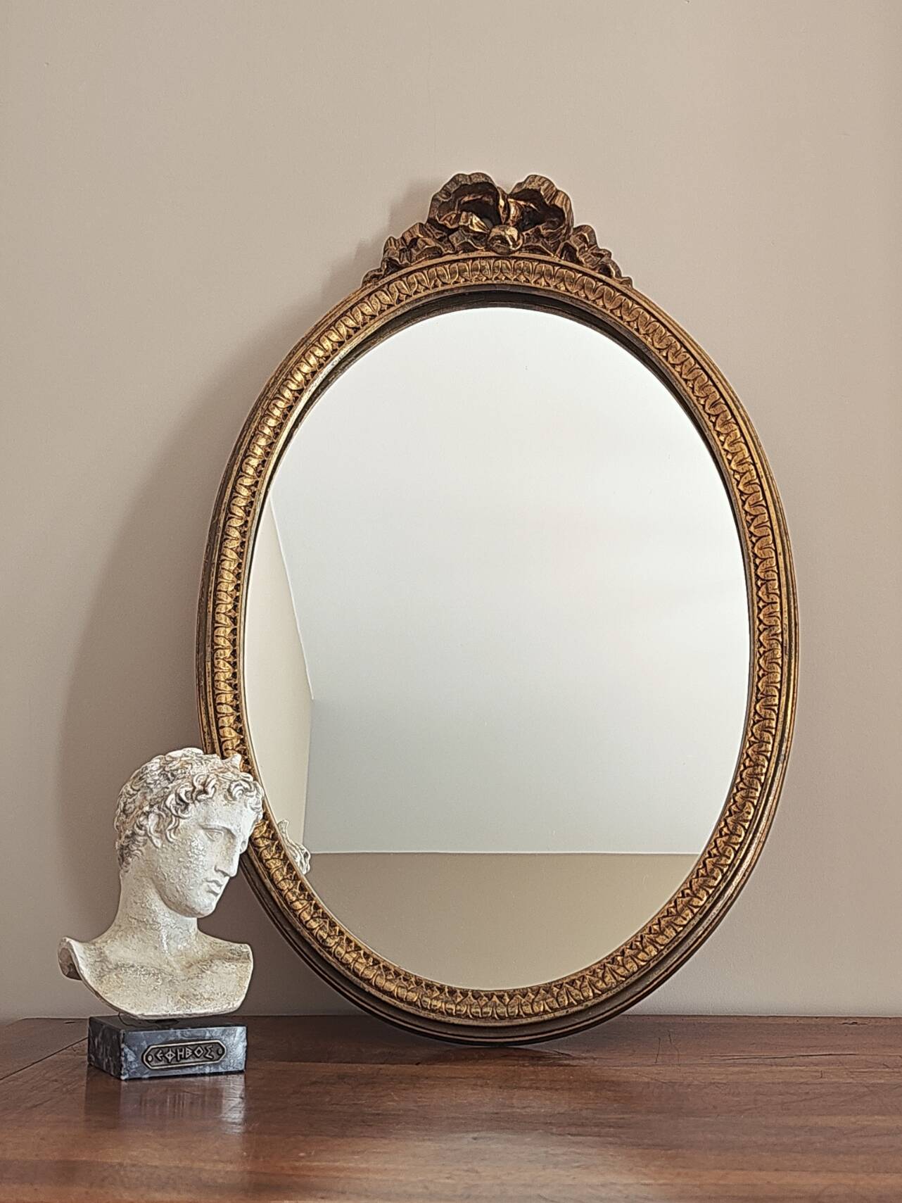 Vintage oval mirror with a carved wooden frame in gold, decorated with a bow.