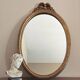 Vintage oval mirror with a carved wooden frame in gold, decorated with a bow.