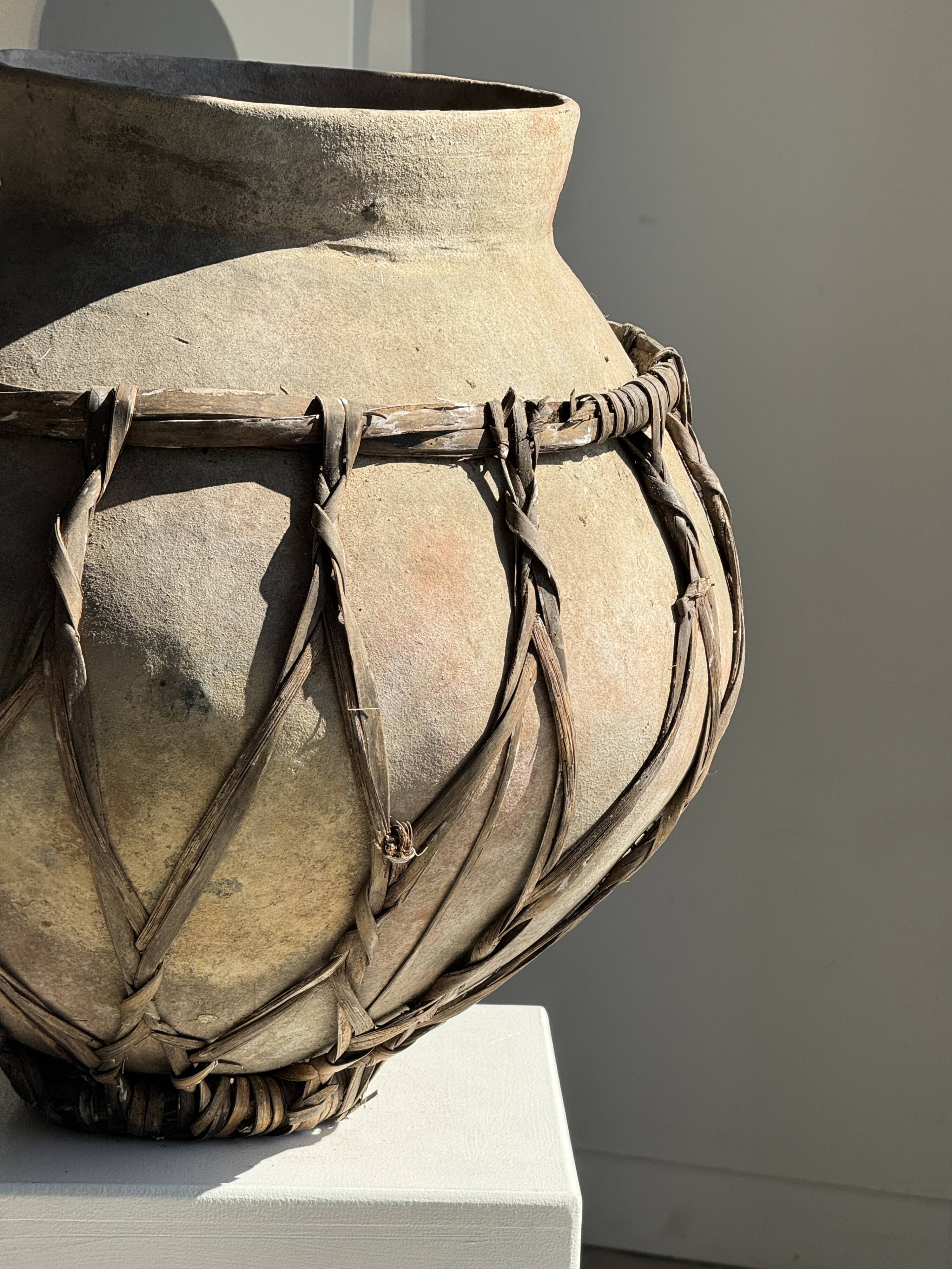 Very large light grey terracotta pot with handles and rattan crossbars.