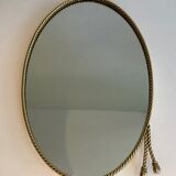Oval brass mirror surrounded by a cord and adorned