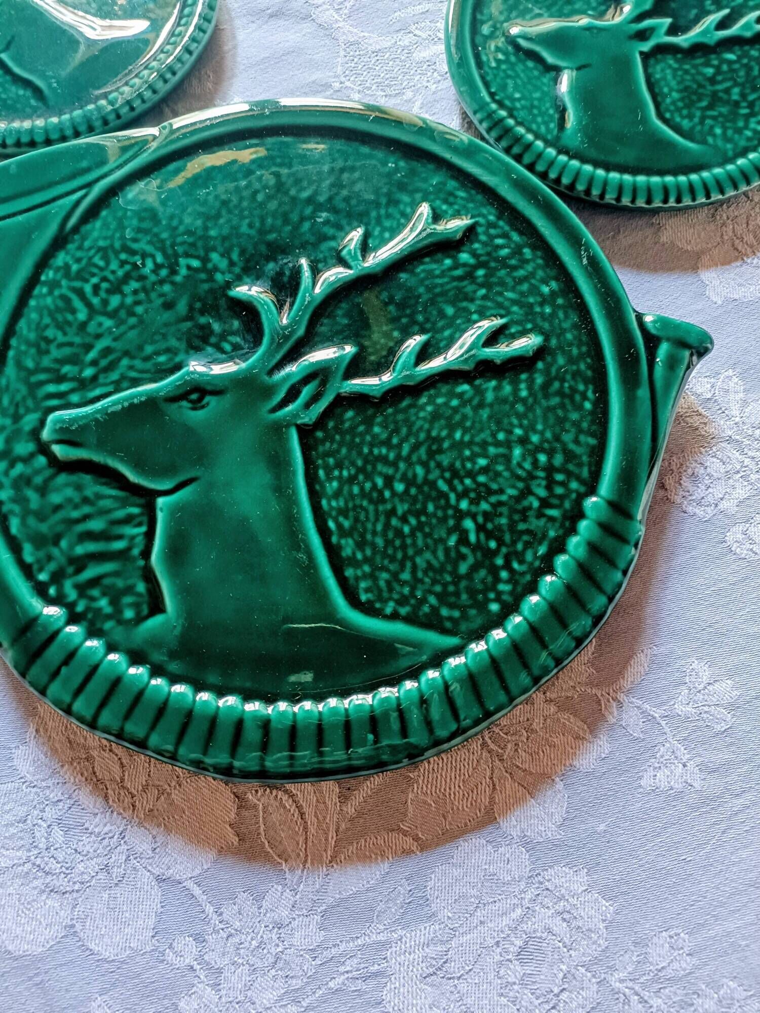 A trivet and two bottle holders in green Vallauris majolica.