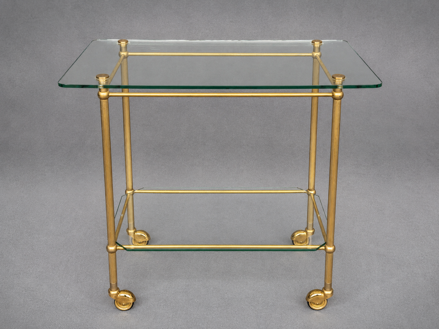 Service trolley on wheels with two glass shelves and a brass frame.