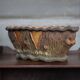Terracotta planter in a brutalist style resembling a tree trunk, pot cover, countryside.