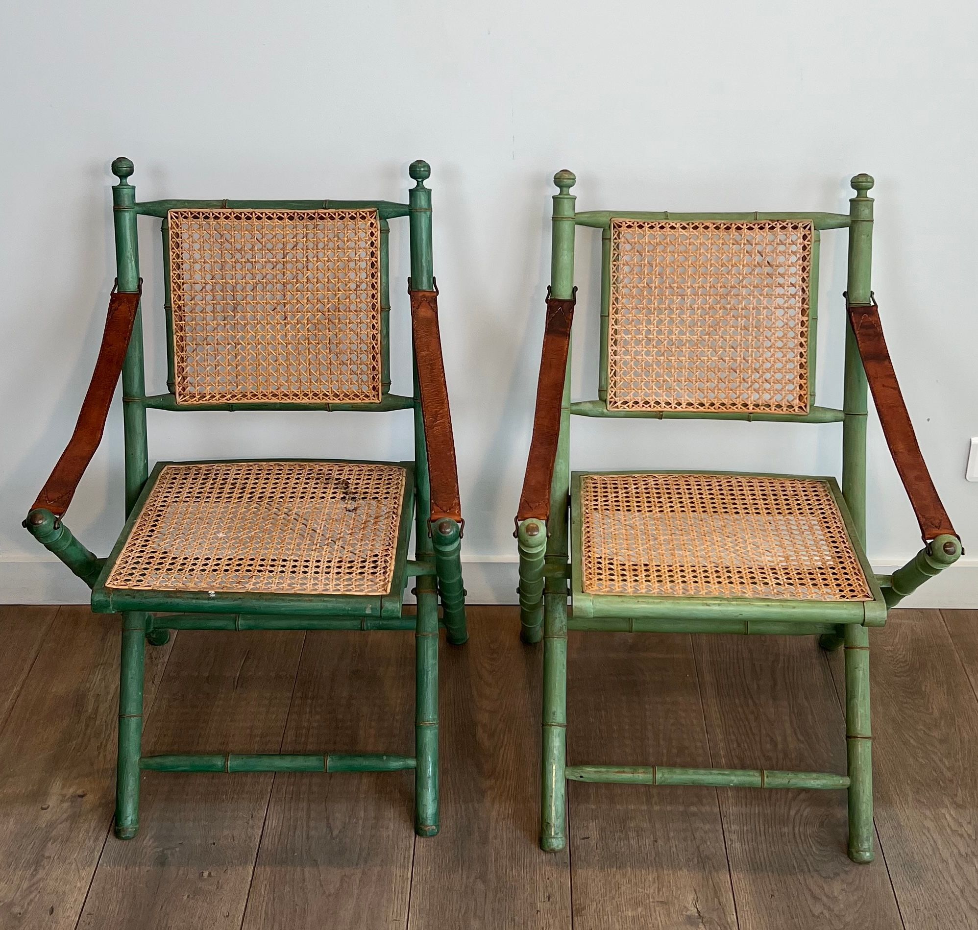 Paire de chaises safari pliantes façon faux-bambou patiné, dossiers et assises cannées et repose-bras en cuir