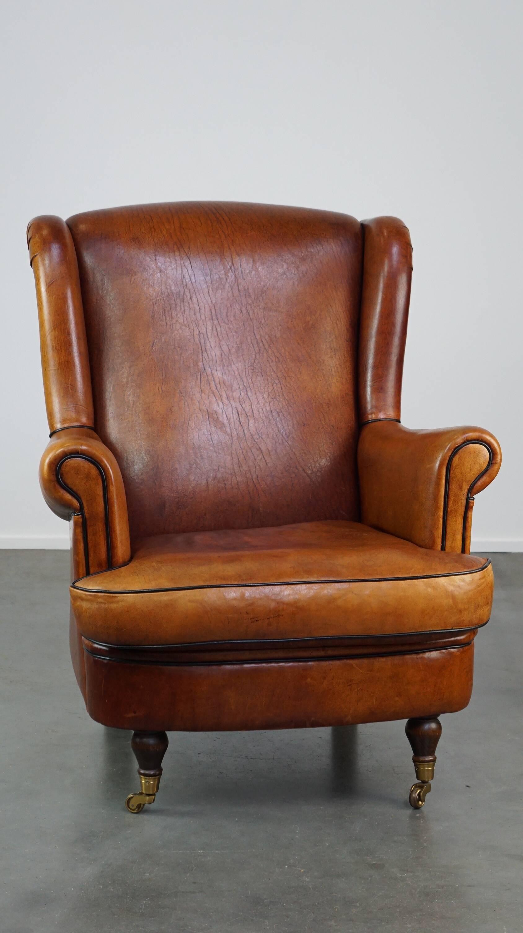 Subtle sheepskin wing chair in good condition on brass front wheels