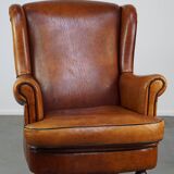 Subtle sheepskin wing chair in good condition on brass front wheels