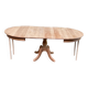 Large extendable round dining table stripped in solid cherry wood with a central leg.