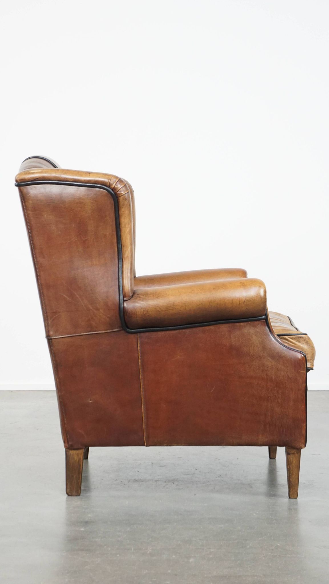 Cognac-colored sheep leather wingback chair finished with black piping