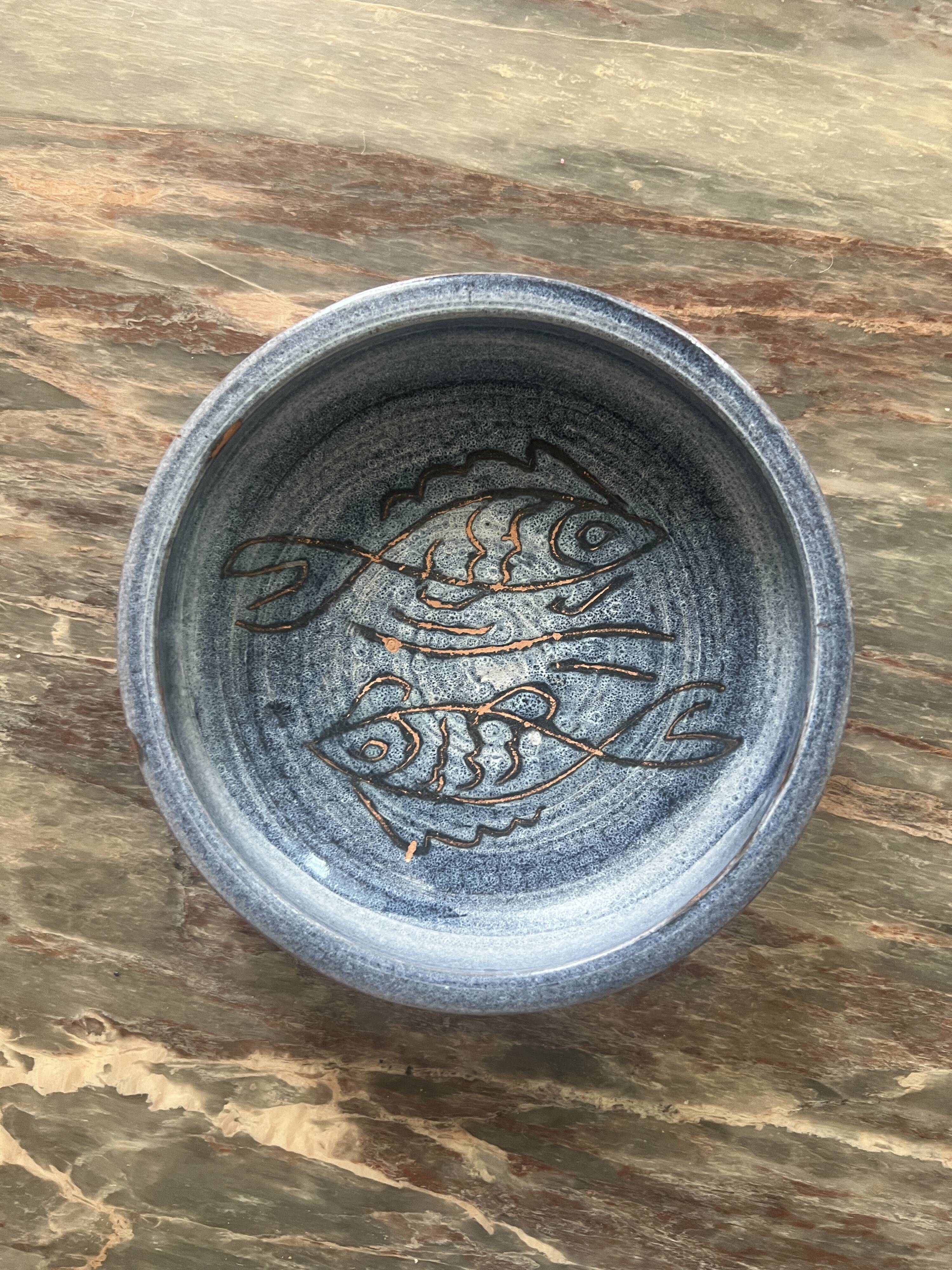 Glazed blue ceramic bowl with stylised fish decoration.