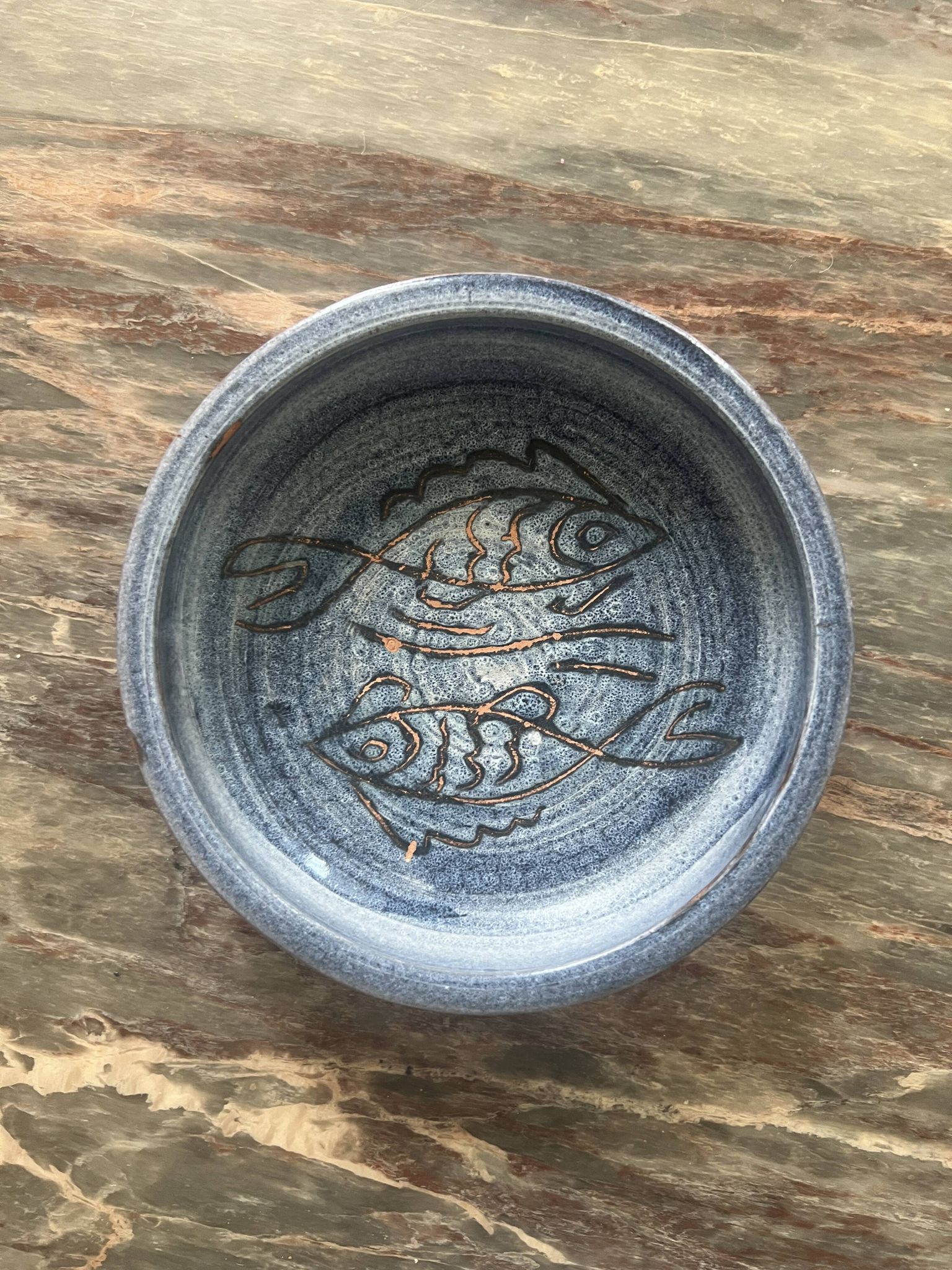 Glazed blue ceramic bowl with stylised fish decoration.