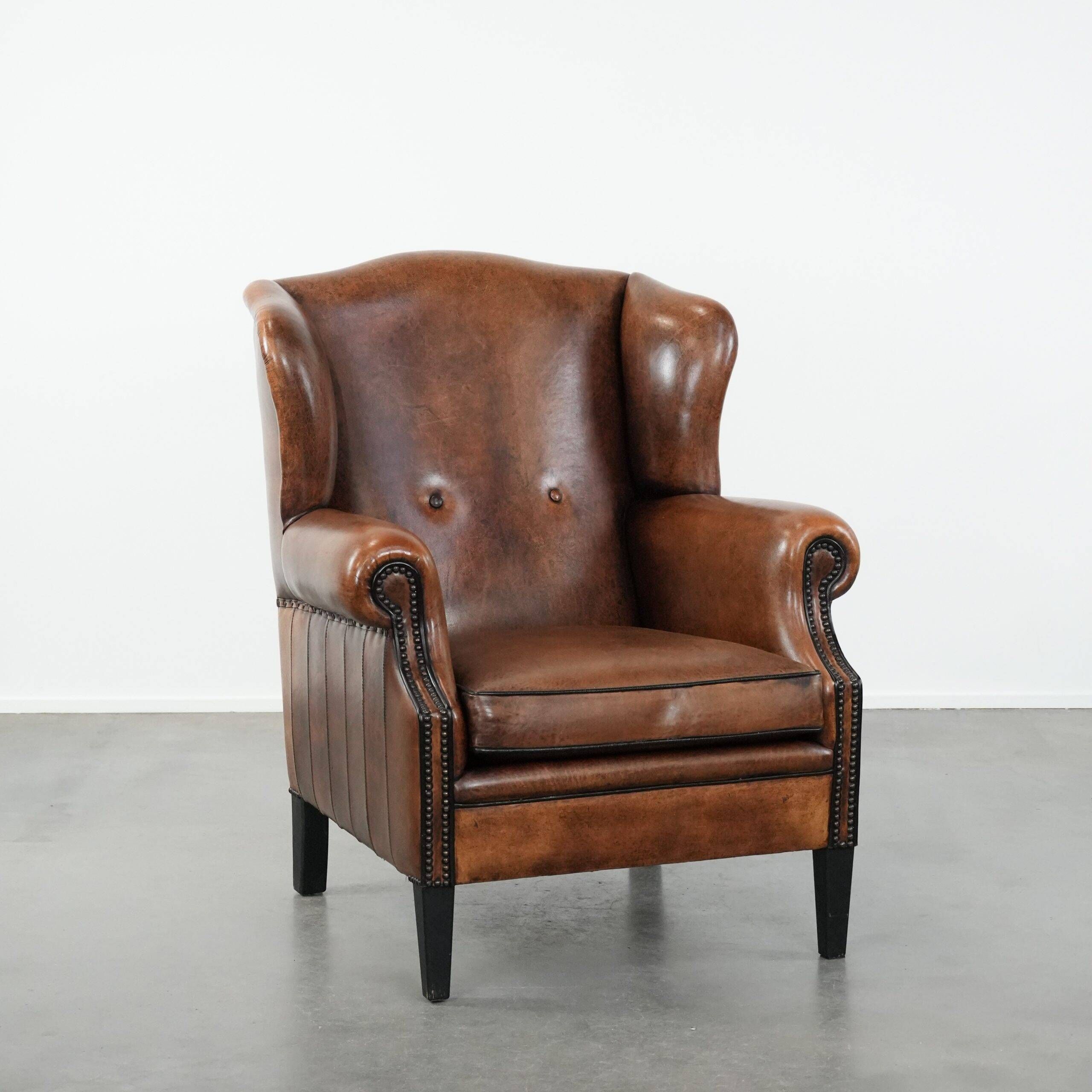 Sheepskin wingback armchair with decorative nails and black piping