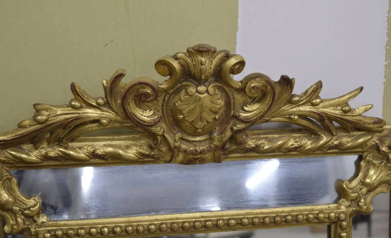 Rectangular glass with a golden frame and a pediment adorned with laurel branches.