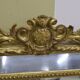 Rectangular glass with a golden frame and a pediment adorned with laurel branches.