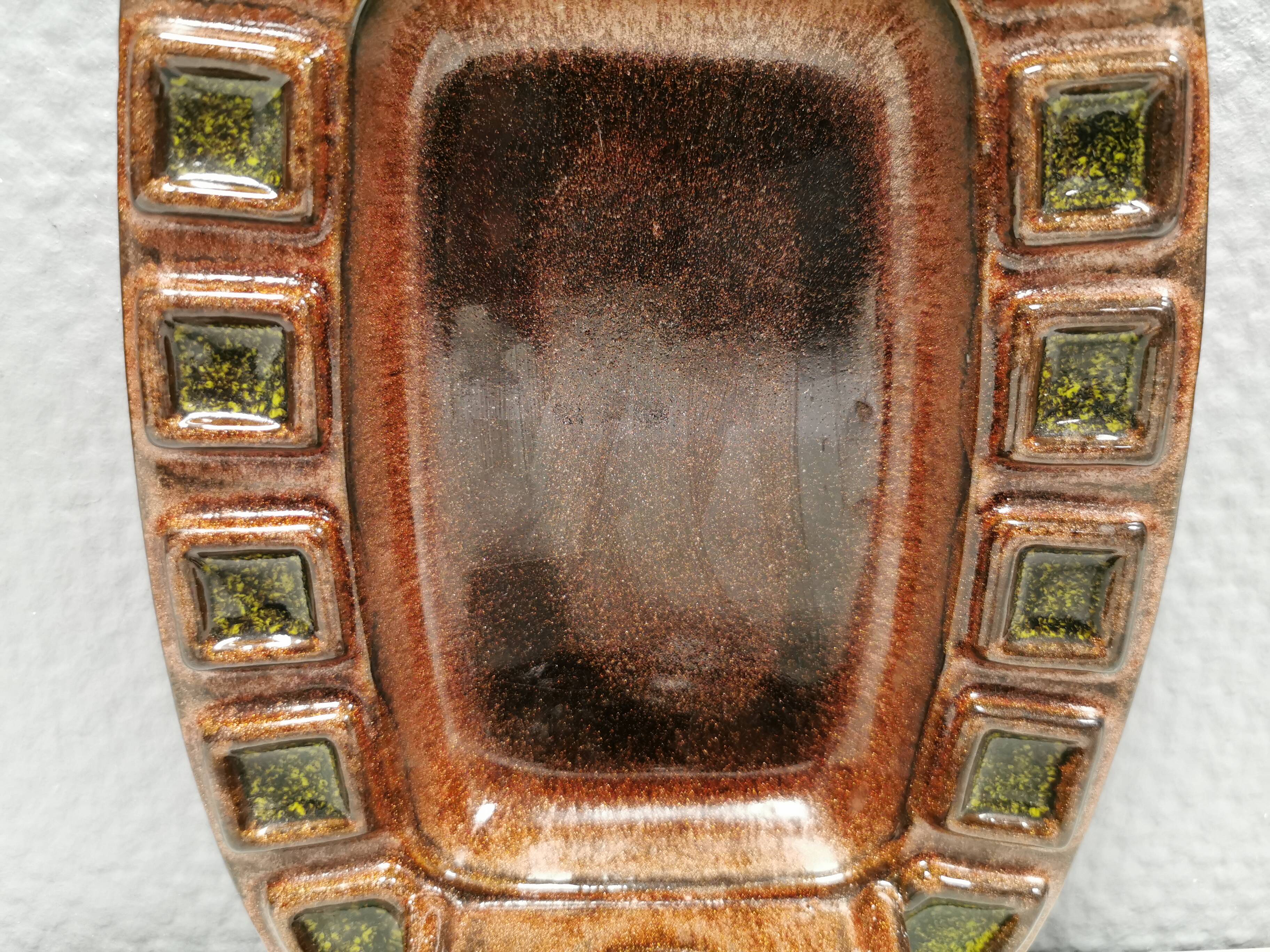 Wall-mounted candleholder in earthy, greenish, golden colours and shades.