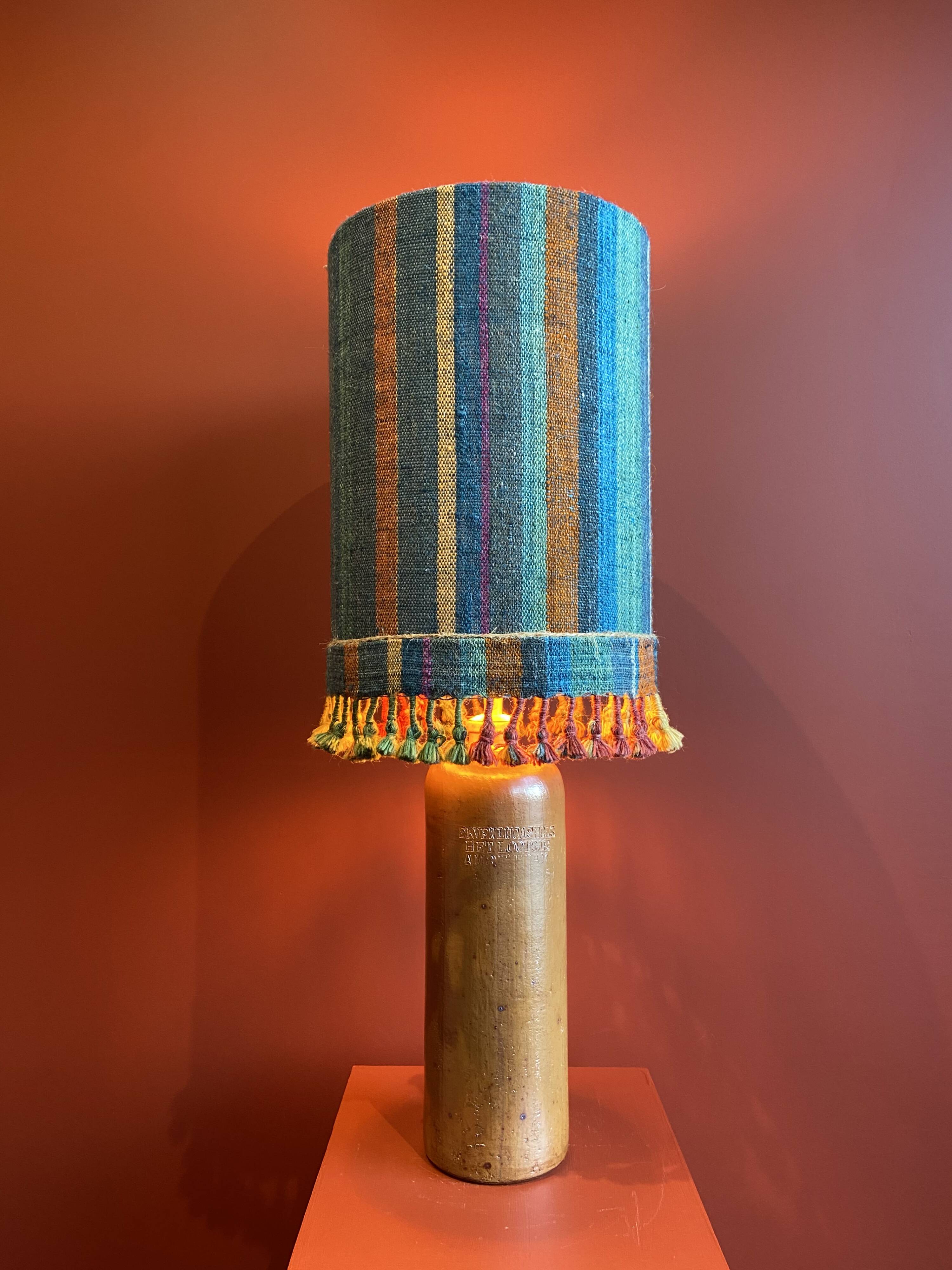 "Stoneware Bottle Lamp" with a multicoloured blue lampshade handwoven in India.