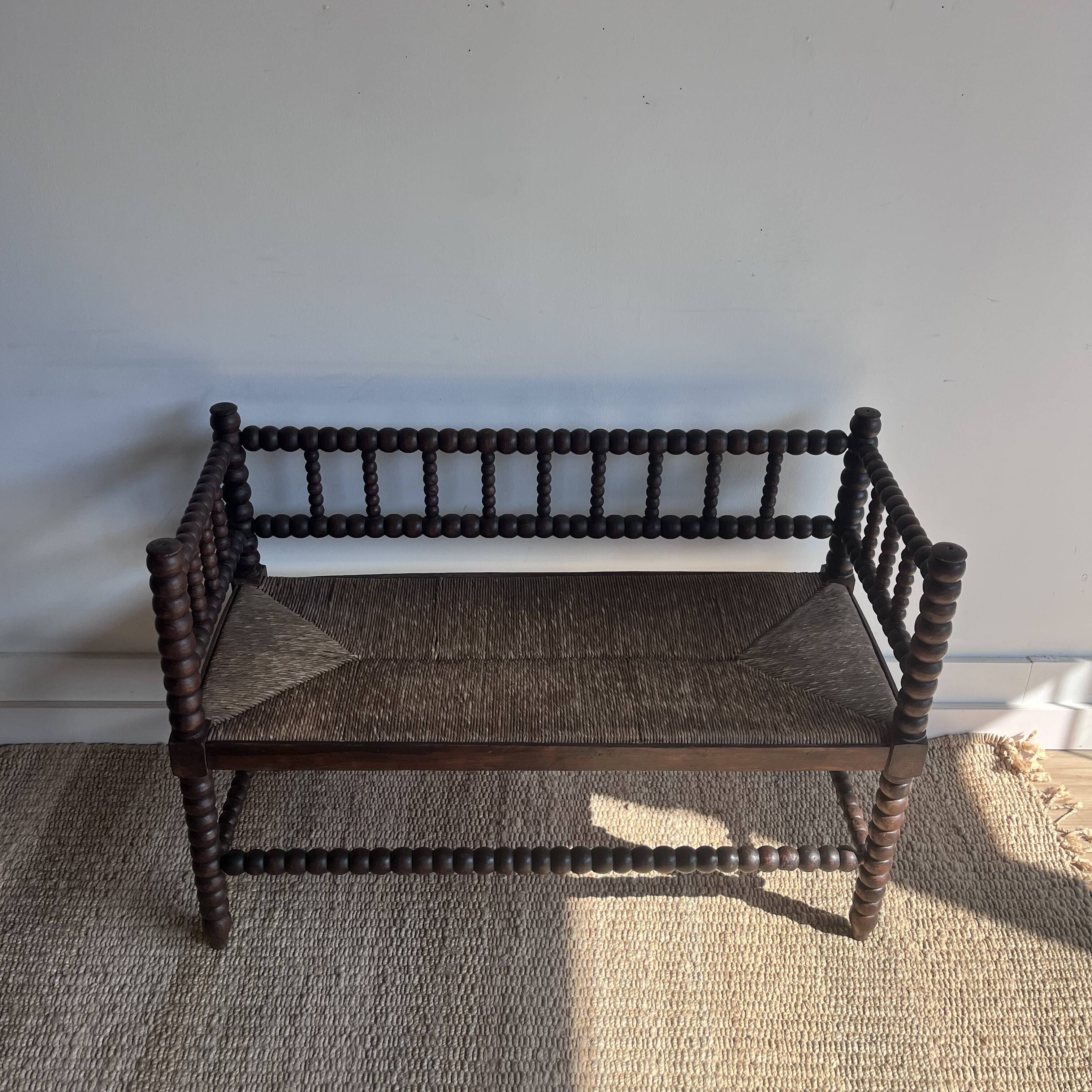 Turned wood bobbin bench with a straw seat.