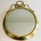 Decorative oval mirror in brass adorned with a large twisted bow.