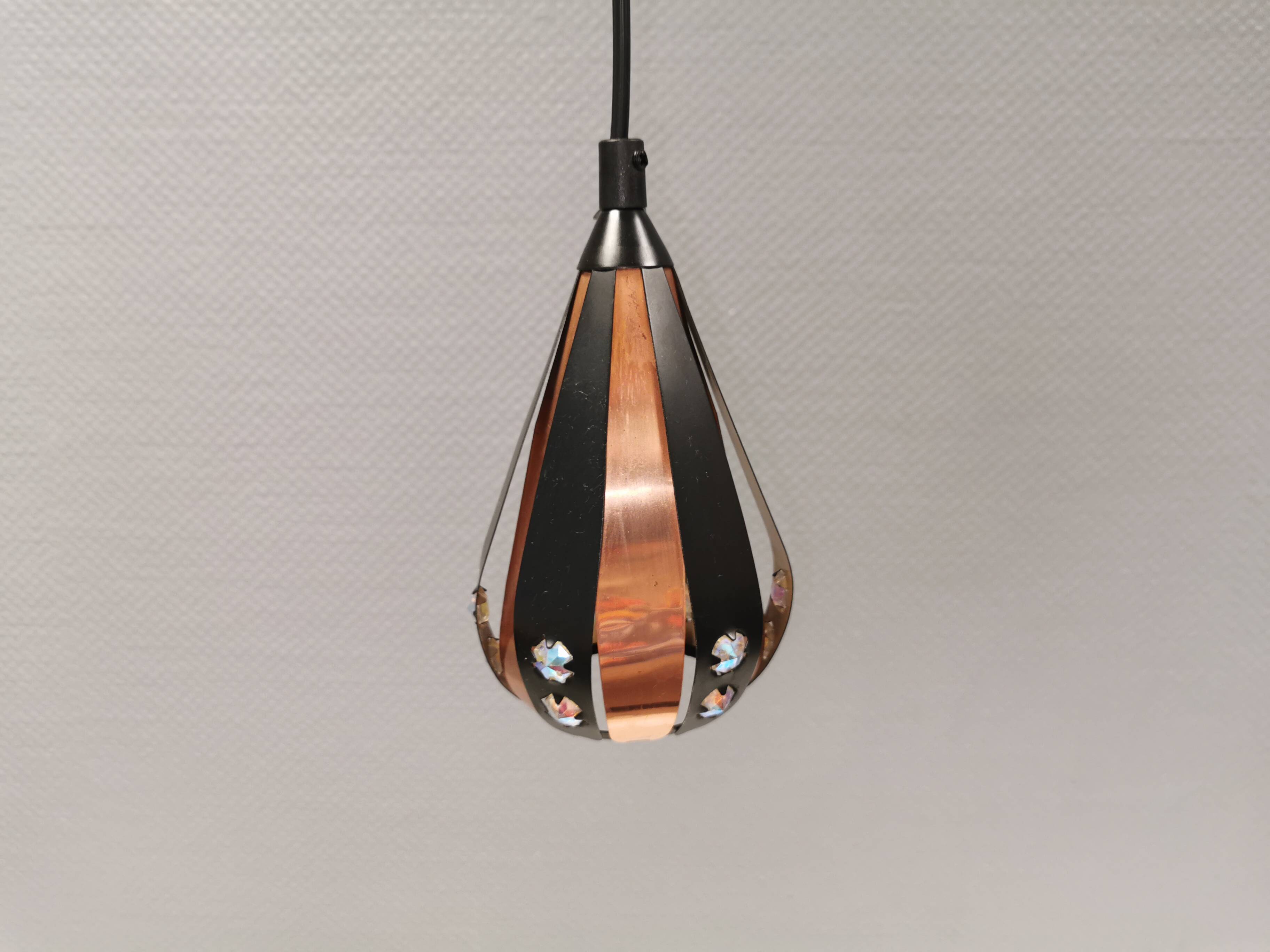 A teardrop-shaped pendant lamp made of copper, black metal, and prisms.