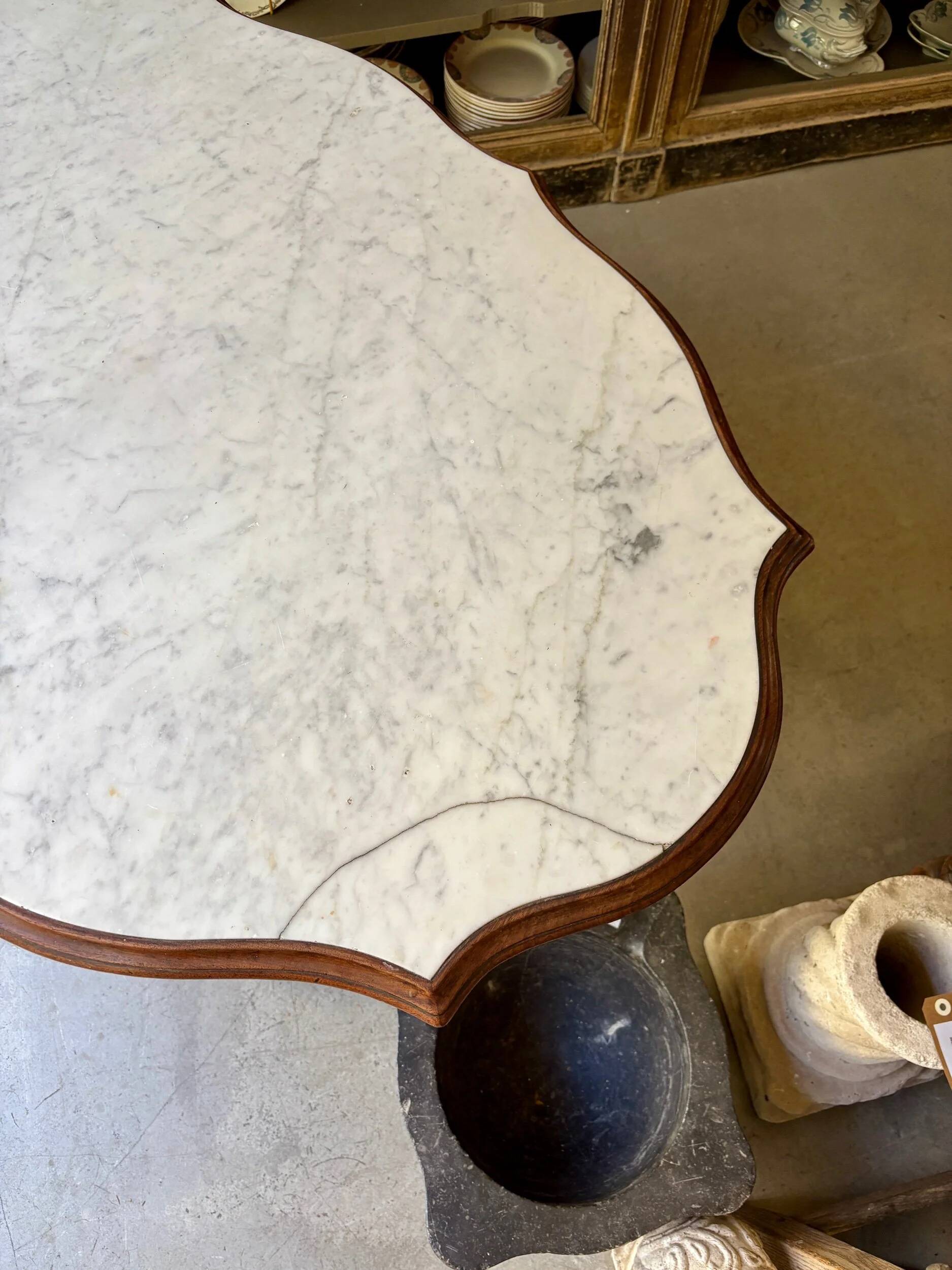 Table with a carved wooden frame and grey marble top on wheels, measuring 130 x 82 cm.