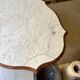 Table with a carved wooden frame and grey marble top on wheels, measuring 130 x 82 cm.