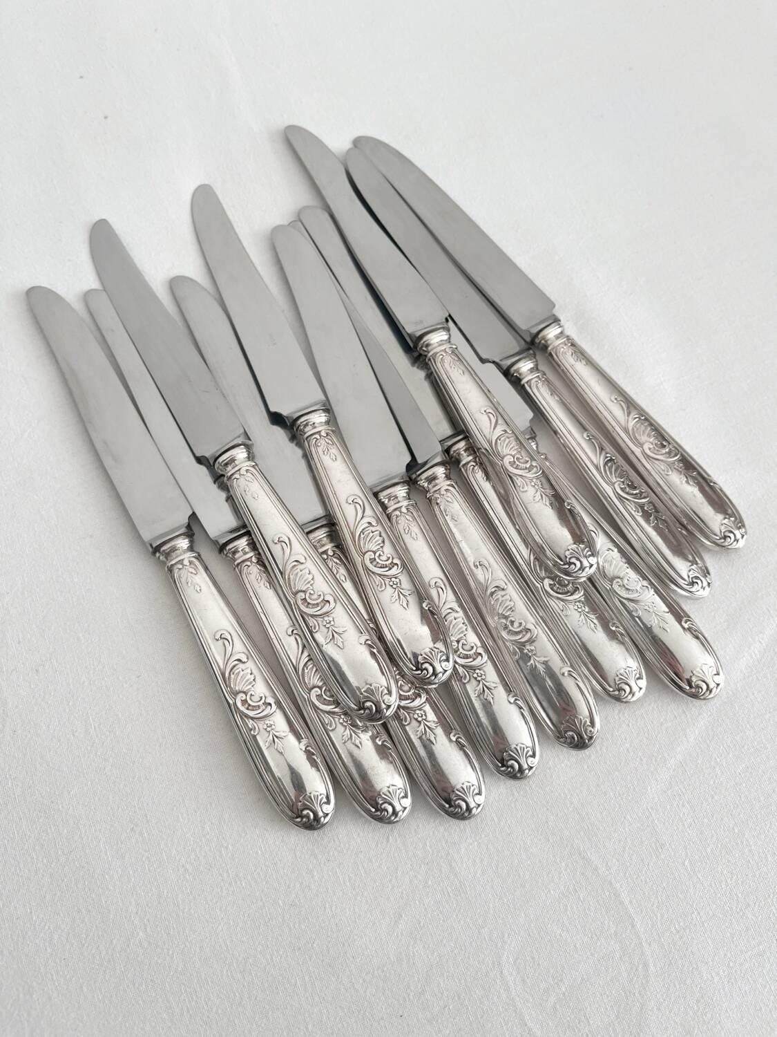 12 antique silver-plated knives with acanthus shell decoration and stainless steel blades.