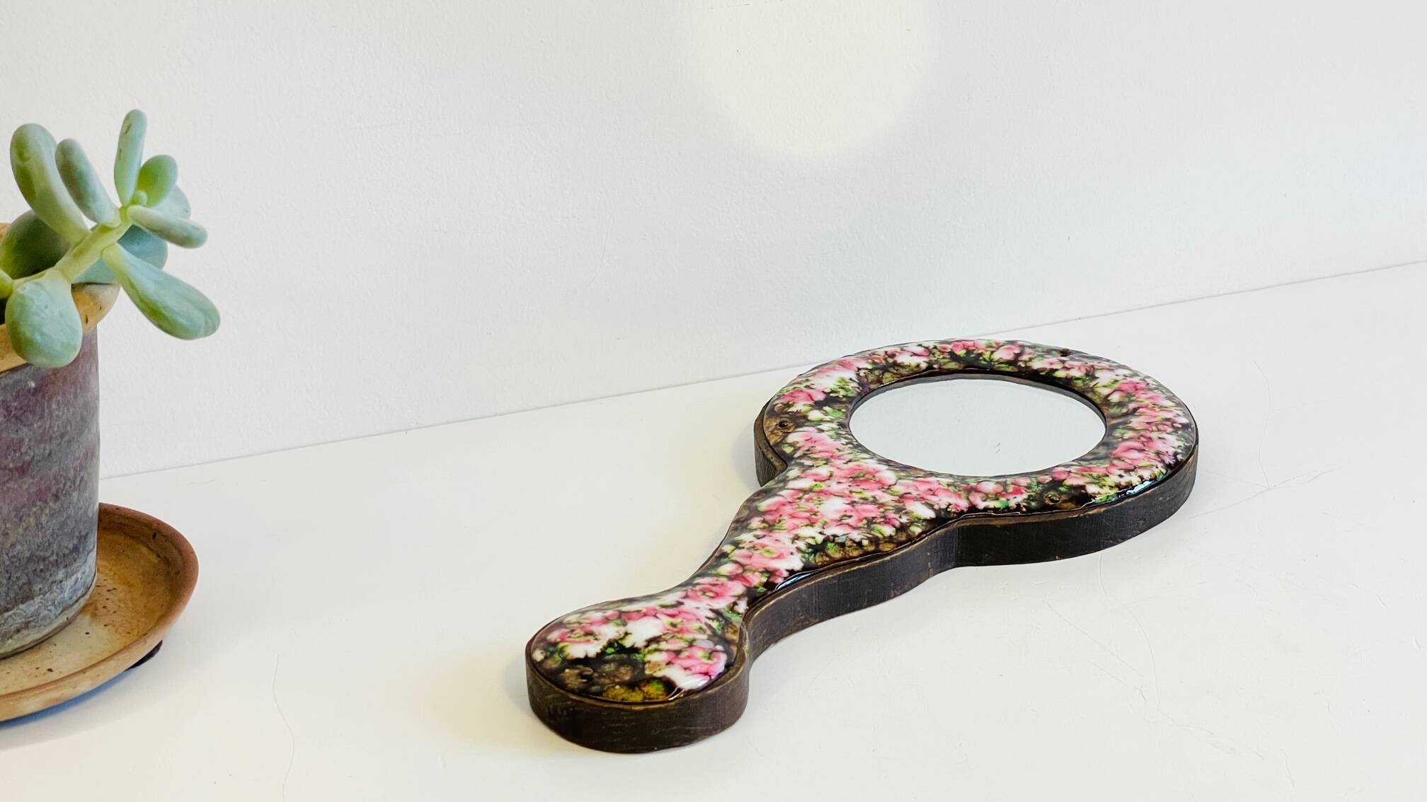 Vintage enameled metal hand mirror on wood