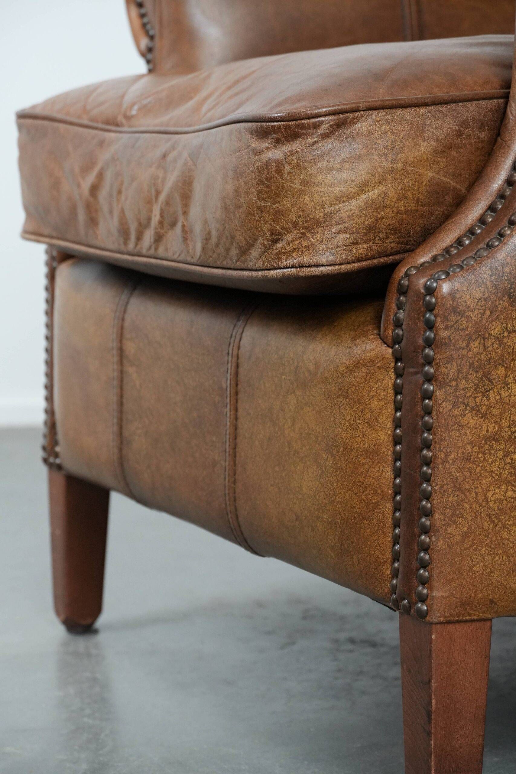 Fauteuil à oreilles de style anglais couleur cognac en cuir de vache.